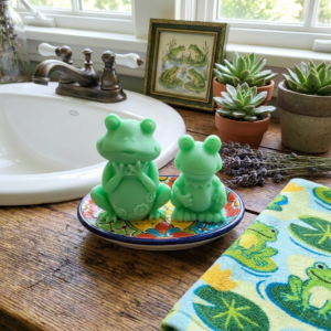 Adorable handmade green frog soaps by The Angelina Store. Two cute and detailed frog-shaped novelty soaps in a vibrant light green color. The larger frog features delicate flower details on its belly while the smaller frog has a charming ruffled collar. Whimsical, high-quality artisan soaps perfect for kids, frog lovers, bathroom decor, or as a fun unique gift.