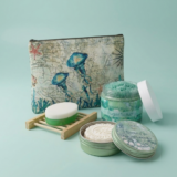 Oceanica Spa Collection gift set by The Angelina Store. Beautifully arranged self-care products featuring the Oceanica Spa Sugar Scrub in a clear jar, Natural Lotion Bar in a green tin, green and white soap bar on a wooden soap dish, and a coordinating jellyfish-themed zip pouch. Serene sea-inspired skincare and bath collection in soft turquoise and green tones, perfect for spa days, relaxation, and thoughtful gifting.