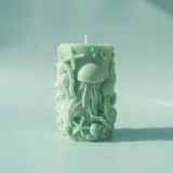 Handcrafted seafoam green sculptural pillar candle from The Angelina Store's Oceanica Spa Collection. Beautiful artisan candle featuring intricate raised ocean life designs including a prominent jellyfish, starfish, seashells, and coral. Calming spa-inspired candle in a soft mint green color, perfect for creating a serene, coastal, and relaxing atmosphere. Premium natural wax candle for meditation, bathroom decor, and ocean-themed home styling.