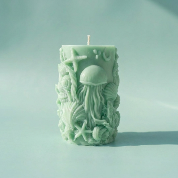 Handcrafted seafoam green sculptural pillar candle from The Angelina Store's Oceanica Spa Collection. Beautiful artisan candle featuring intricate raised ocean life designs including a prominent jellyfish, starfish, seashells, and coral. Calming spa-inspired candle in a soft mint green color, perfect for creating a serene, coastal, and relaxing atmosphere. Premium natural wax candle for meditation, bathroom decor, and ocean-themed home styling.