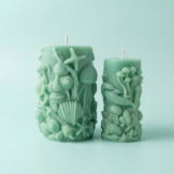 Handcrafted seafoam green sculptural pillar candle from The Angelina Store's Oceanica Spa Collection. Beautiful artisan candle featuring intricate raised ocean life designs including a prominent jellyfish, starfish, seashells, and coral. Calming spa-inspired candle in a soft mint green color, perfect for creating a serene, coastal, and relaxing atmosphere. Premium natural wax candle for meditation, bathroom decor, and ocean-themed home styling.