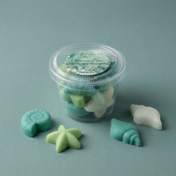 Oceanica Spa Organic Soy Wax Melts by The Angelina Store. Beautiful clear container filled with premium organic soy wax melts, surrounded by individual shaped melts including a starfish, nautilus shell, and conch shell. Part of the calming Oceanica Spa Collection with soothing sea-inspired fragrances. Natural home fragrance wax melts perfect for wax warmers and creating a relaxing coastal atmosphere.
