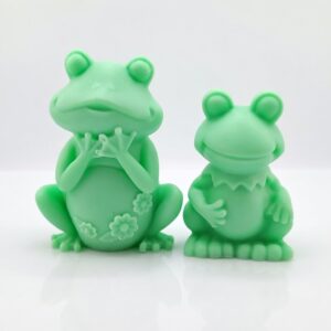 Adorable handmade green frog soaps by The Angelina Store. Two cute and detailed frog-shaped novelty soaps in a vibrant light green color. The larger frog features delicate flower details on its belly while the smaller frog has a charming ruffled collar. Whimsical, high-quality artisan soaps perfect for kids, frog lovers, bathroom decor, or as a fun unique gift.