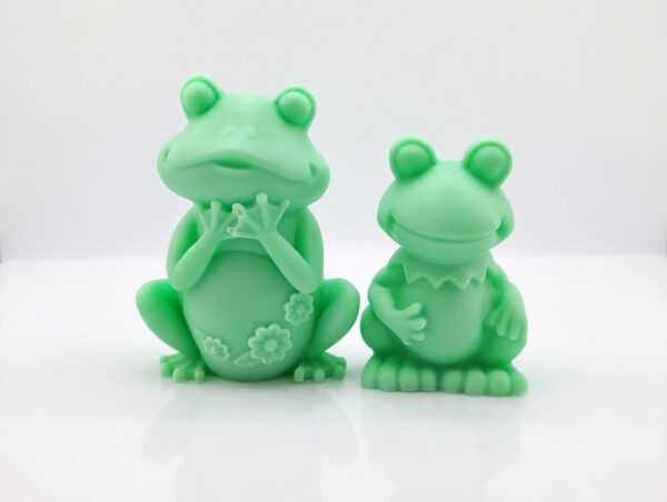 Adorable handmade green frog soaps by The Angelina Store. Two cute and detailed frog-shaped novelty soaps in a vibrant light green color. The larger frog features delicate flower details on its belly while the smaller frog has a charming ruffled collar. Whimsical, high-quality artisan soaps perfect for kids, frog lovers, bathroom decor, or as a fun unique gift.
