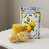 Limoncello Crème Soap & Candle Gift Set by The Angelina Store. Bright and cheerful collection featuring a vibrant yellow bubble texture pillar candle, two hyper-realistic lemon-shaped soaps (one beautifully wrapped with signature label), and a coordinating lemon-themed gift bag. Fresh, zesty Limoncello Crème scented soaps and candles with natural citrus fragrance, perfect for kitchen, bathroom, or as a luxurious summer gift. Bright, sunny, and inviting handmade lemon gift set.